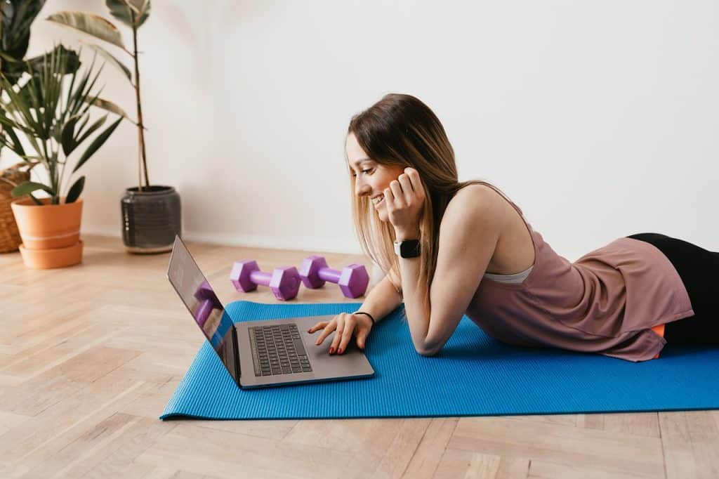 typing on a laptop while lying on a yoga mat with weights on the side