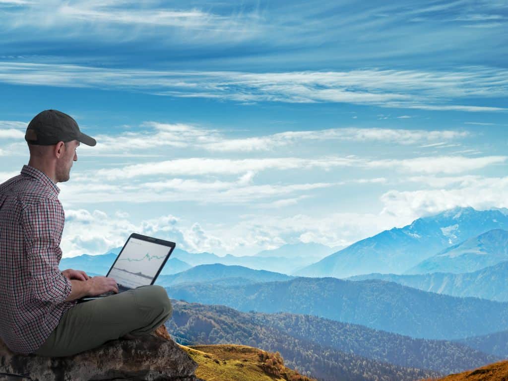 a man on his laptop sitting overlooking a hill