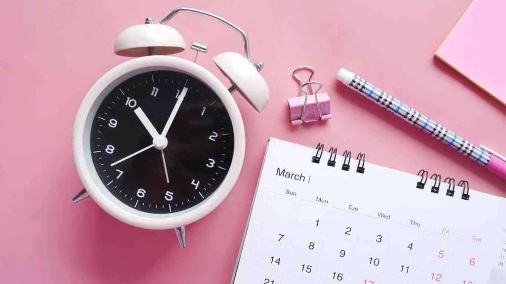 The Best Times To Post On Social Media: A Guide For Maximum Engagement - A clock, calendar pen, clip and paper on a pink background