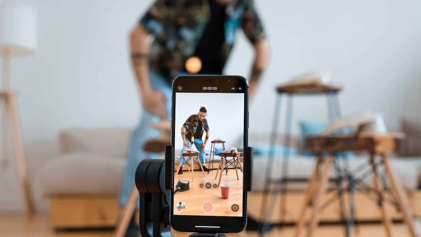 A smartphone filming a man playing the drums in a home setting.