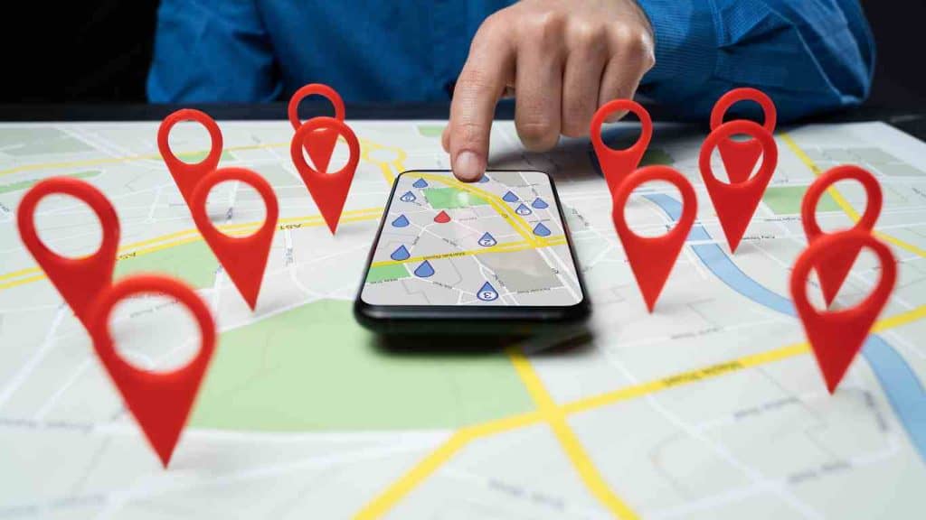 A person pointing at a smartphone map surrounded by location pin