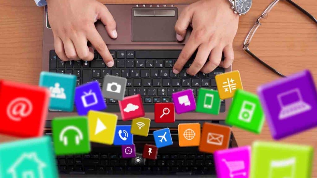 Hands typing on a laptop with colorful social media icons floating, symbolizing social media engagement.