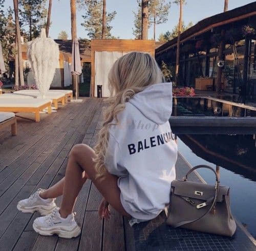 Lady sitting by a pond in her Balenciaga shoes, hoodie and bag