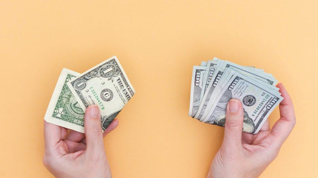 Copywriting Versus Social Media Management: An overhead shot shows two hands one grasping a few dollar bills and the other holding a stack of hundred-dollar bills, all against a vivid background. Perfect for financial themes.