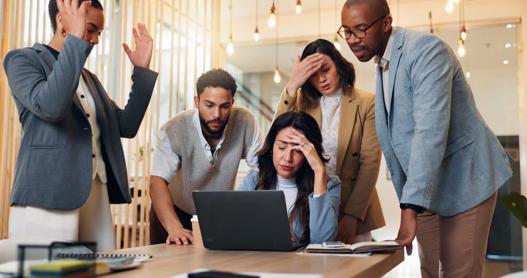 4 co-workers lamenting on the mistake discovered by the boss sitting down in front of her laptop