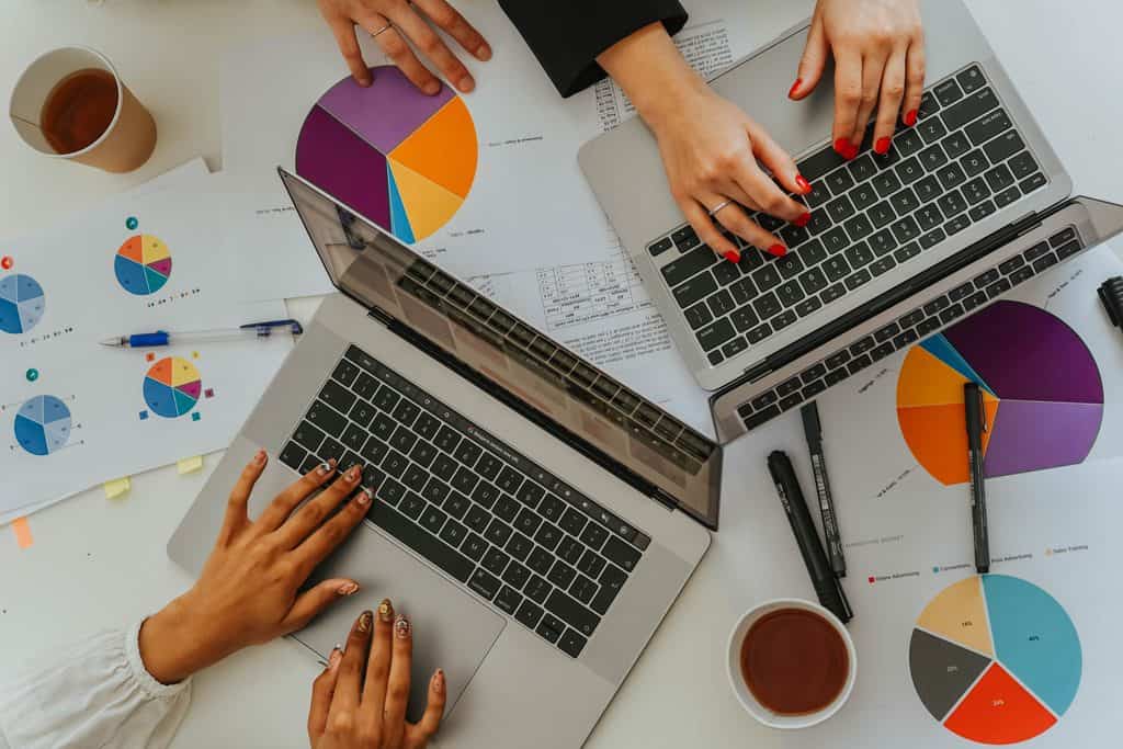 Two people working on laptops beside printed marketing charts and pie graphs