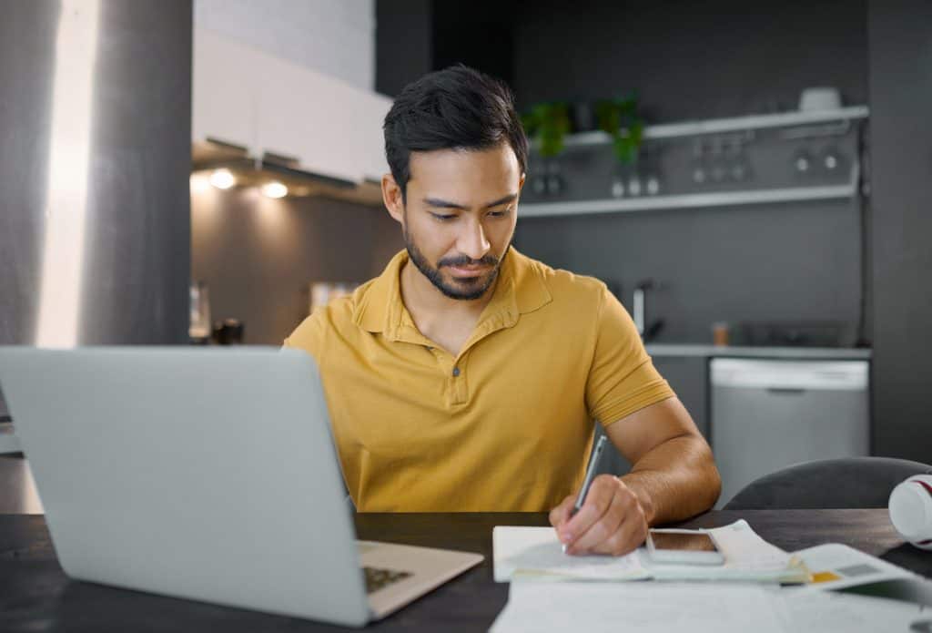 Freelance writer researching and taking notes beside a laptop