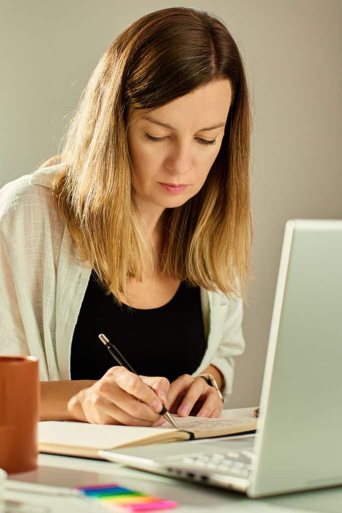 Freelance writer working on a laptop and taking notes at home