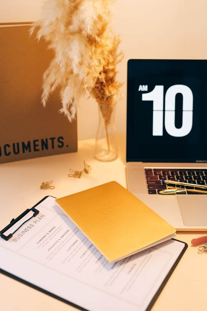 Business plan document on a clipboard beside a laptop and notebook on a warm-toned desk