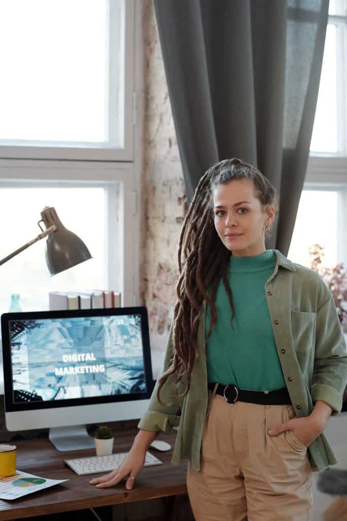 Freelance digital marketer standing at her home-office desk beside a computer screen