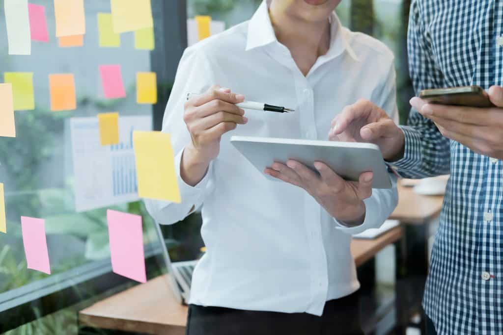 Two people reviewing a tablet beside a sticky-note planning wall, following a freelance business starter guide process