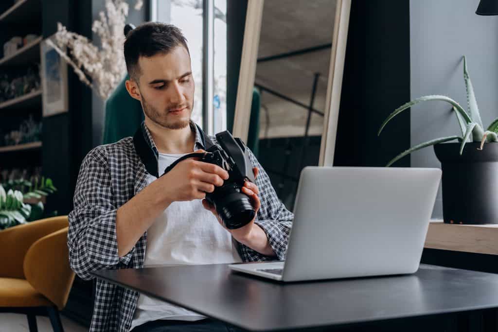 Freelance photographer reviewing work on a camera beside a laptop at a desk