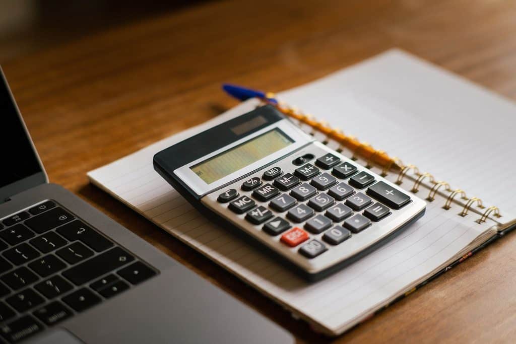 Calculator, open laptop, and notebook on a wooden desk while planning what skills pay online