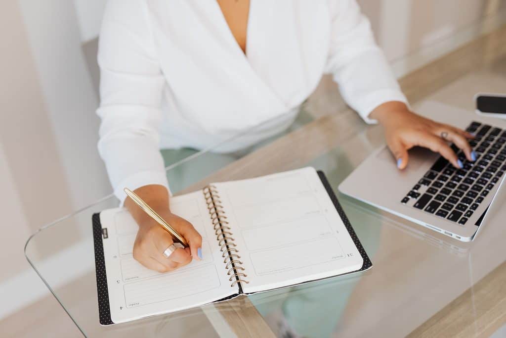 Freelancer writing in a weekly planner next to a laptop while comparing skill options.