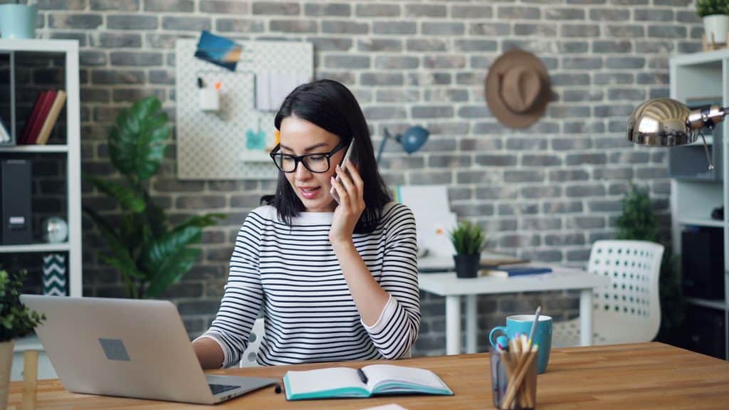 Freelancer talking to a client on the phone at her laptop while discussing how to raise freelance rates