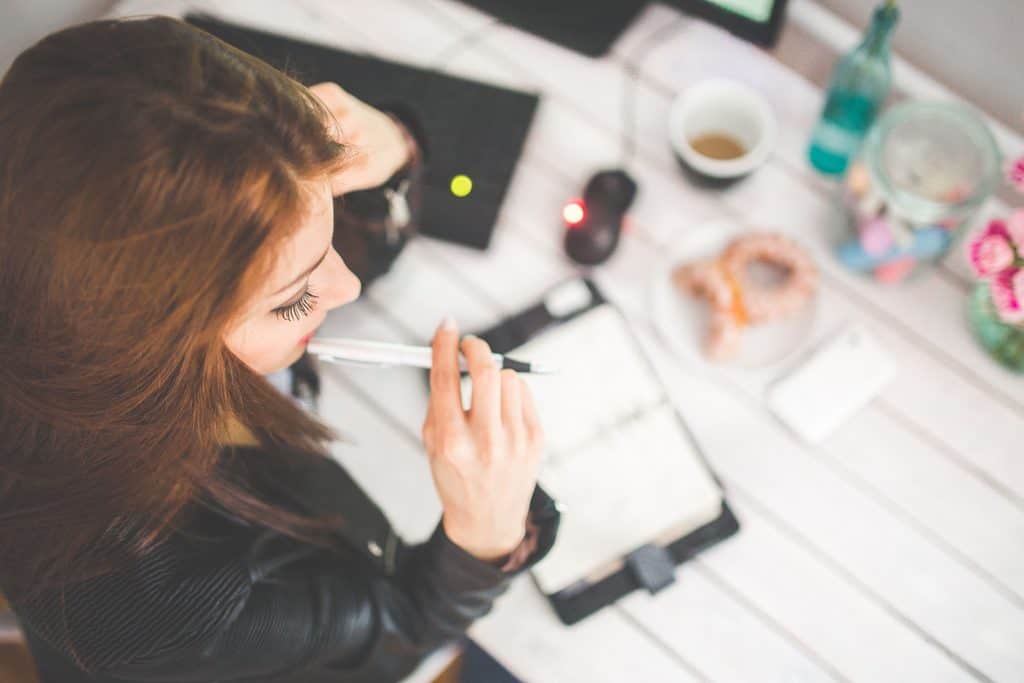 Freelancer pausing to think with a pen over a notebook at a cluttered desk