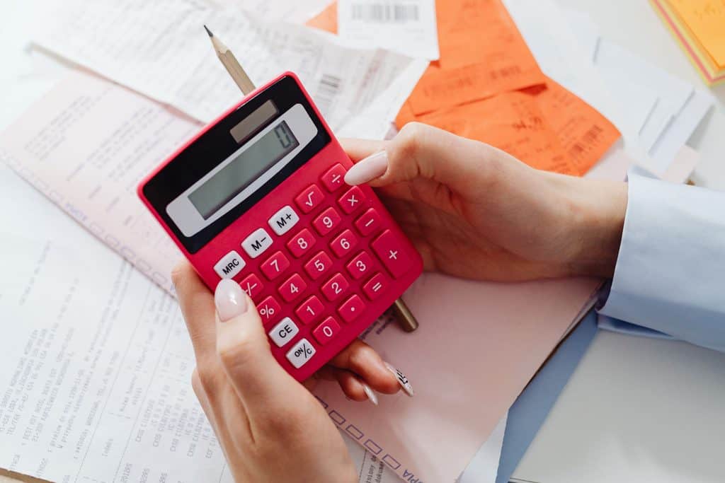 Hand using a calculator over receipts and documents to work out how to price retainer services from a cost floor