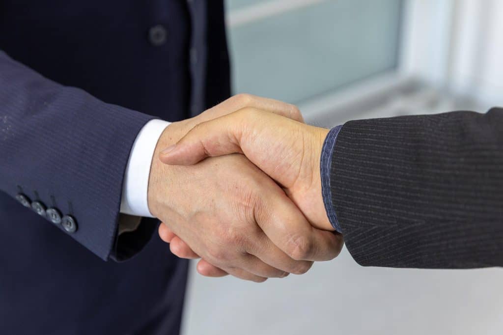 Close-up of two professionals shaking hands to confirm a monthly retainer agreement