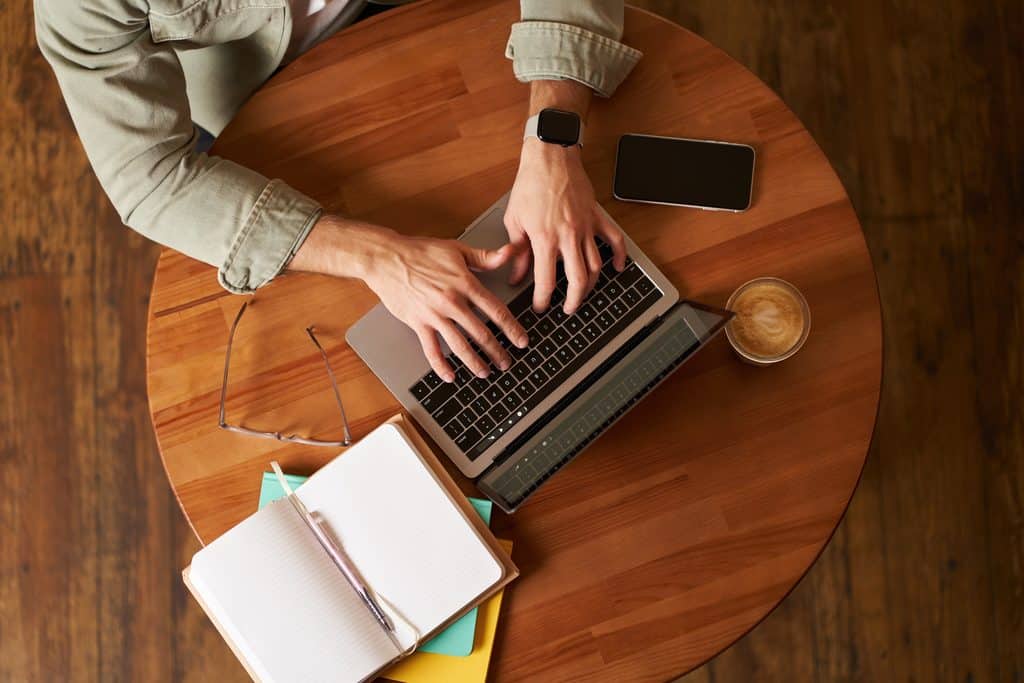 Person working on a laptop at a cafe table, applying answer engine optimization to their website content