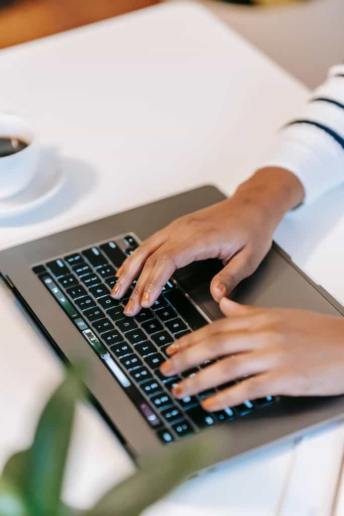 Close-up of hands typing on a laptop beside a coffee cup on a white desk