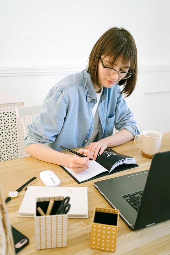 Freelancer writing in a planner beside a laptop at her desk