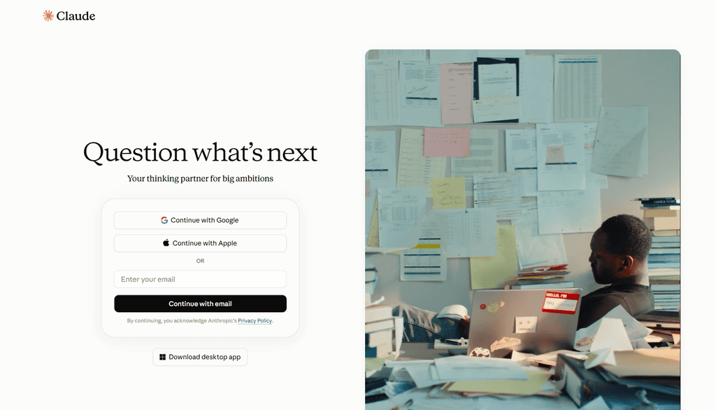 Screenshot of the Claude sign-in page with the tagline "Question what's next, your thinking partner for big ambitions" next to an image of a person working at a cluttered desk covered in notes.