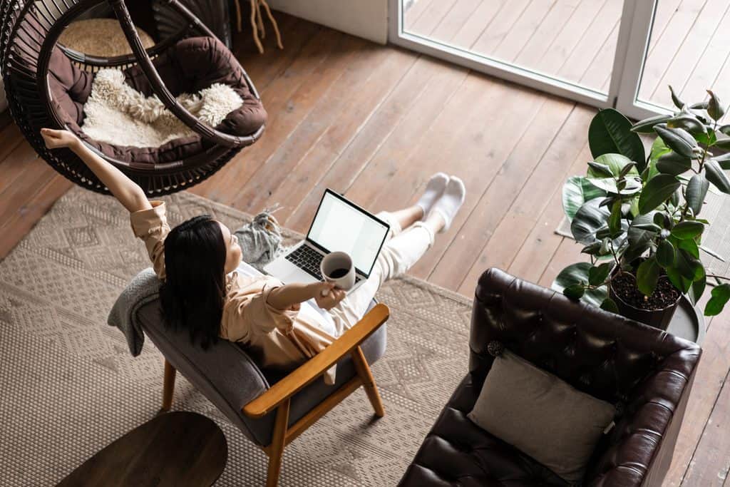 Woman relaxing in a chair with a laptop and coffee mug at home.