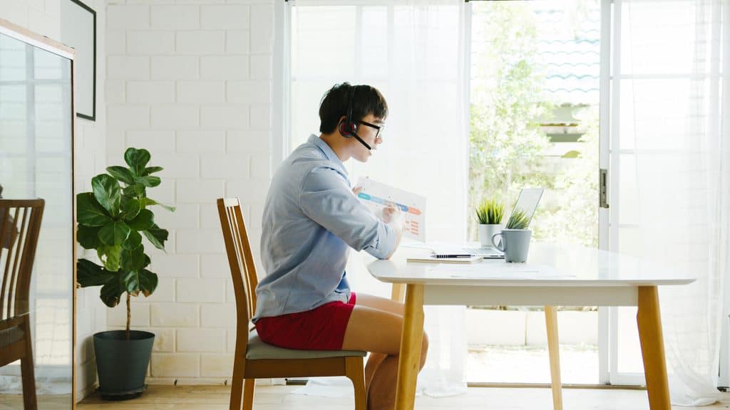 Man in a headset on a video call working from home at a dining table in casual clothing