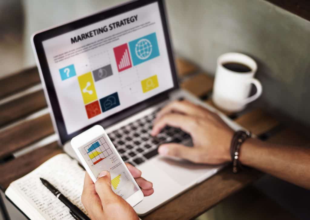 Person reviewing a marketing strategy on a laptop and phone, planning a copywriting course for freelancers path