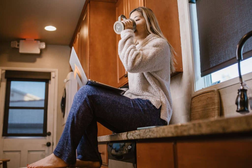 A girl drinking from a cup with a laptop on her lap - presumably a freelancer online, in line with this article - Is Upwork worth it.