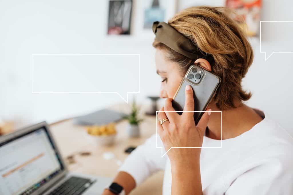 Freelancer taking a client call on her phone beside a laptop at a home desk