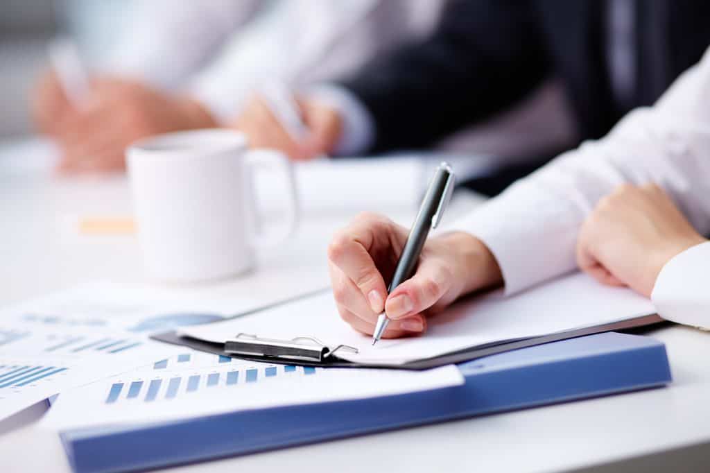 Close-up of a person writing notes on a clipboard beside printed charts