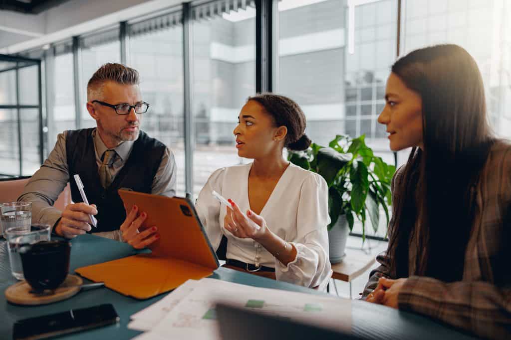 Business team reviewing financial plans together using a laptop and digital tablet in a modern office lounge